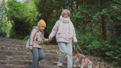 mother gently holds daughter hand while walking carefully down stone staircase in leafy autumn garden guiding dog on leash surrounded by green foliage in peaceful moment of family bonding