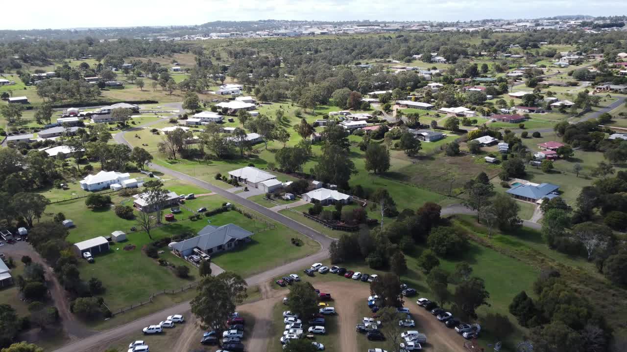 4K aerial video of an unpaved grassy carpark and private properties with large family homes
in a regional town in Australia