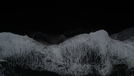 top down of waves crashing on the south coast of iceland with black sands, aerial