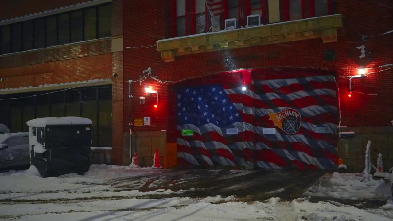 Accumulo di neve sull'ingresso di una caserma dei pompieri con porte a murale a bandiera. Vista a livello del suolo di una stazione dei pompieri durante una tempesta di neve con neve abbondante a terra e facciata dell'edificio a New York