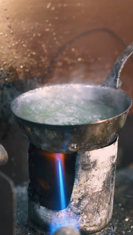cu: jeweler uses gas burner to heat green liquid to process decorative item on table near metal sheet in workshop closeup