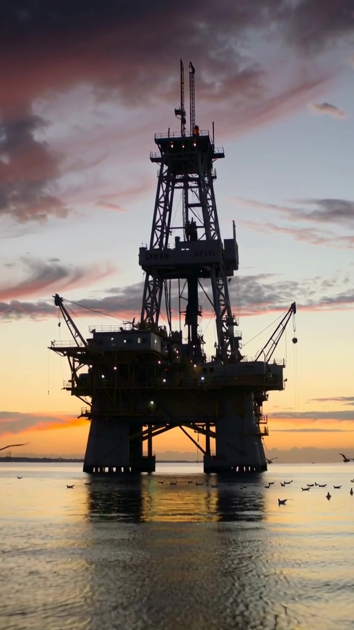 Vertical video: Shifting sunset light bathing offshore drilling platform at sea, seabirds flying