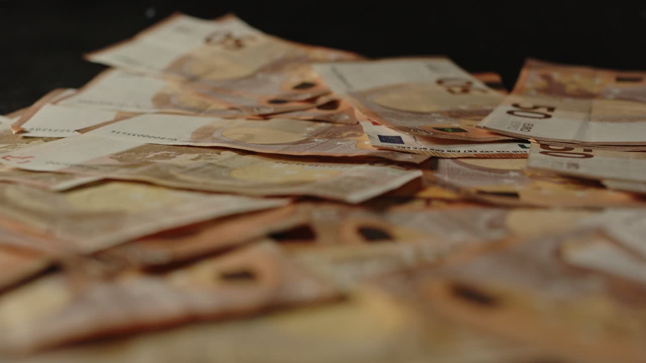 Dolly-Aufnahme einer großen Menge Bargeld mit verstreuten 50-Euro-Scheinen auf einer schwarzen Oberfläche.