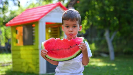 beautiful caucasian toddler eating a slice of a big watermelon. cute kid having a healthy snack with juicy berry outdoors in summer. blurred backdrop.
