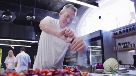 cocinero profesional caucásico vestido de blanco en una cocina de un restaurante, condimentando comida
