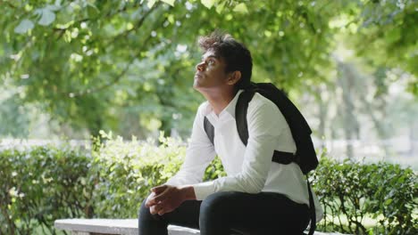 Sad-young-man-sitting-on-bench-at-city-park-observe-surroundings,-static