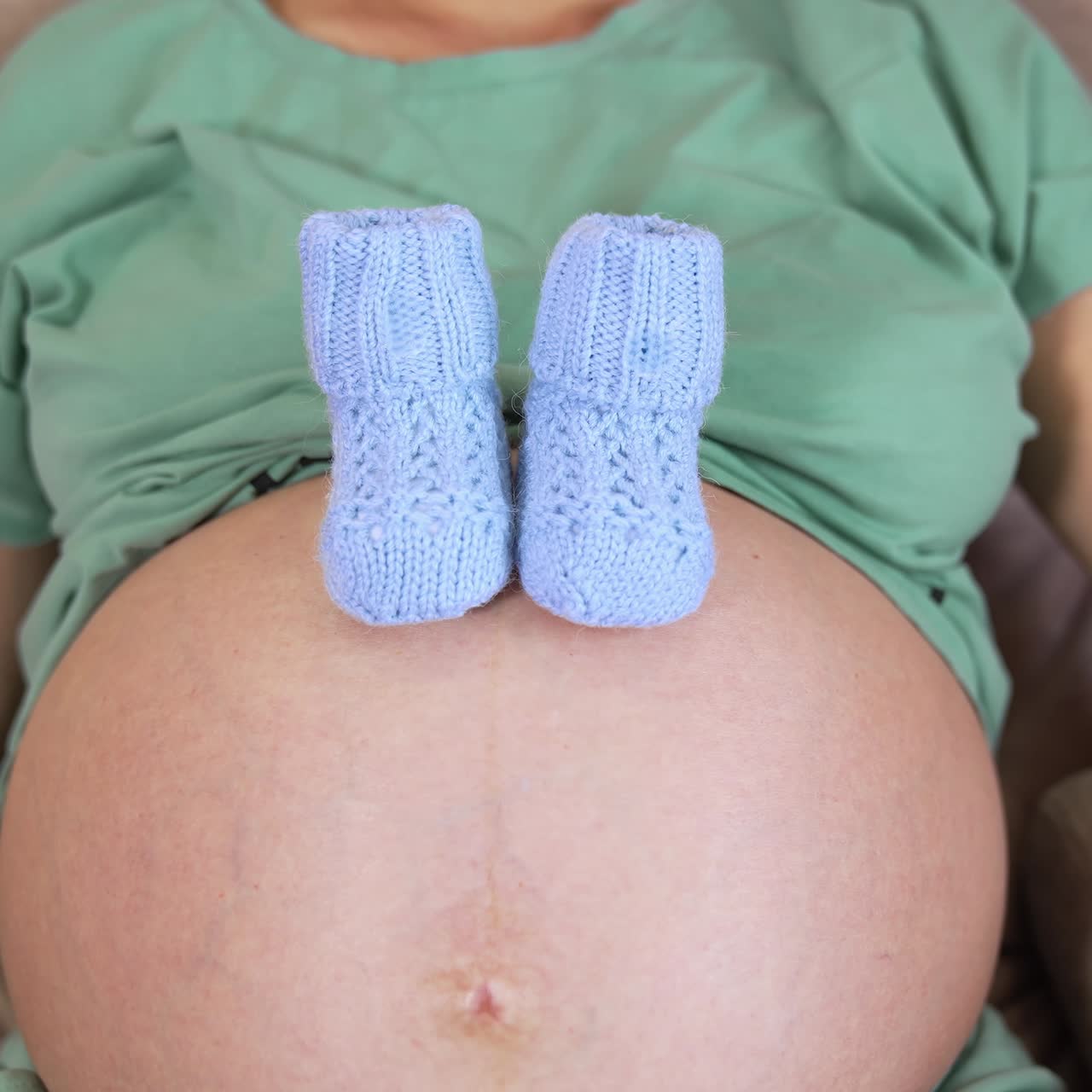 Calzini di lana sulla pancia scoperta di una futura mamma. Donna incinta sdraiata su un divano che mostra dei piccoli calzini blu sulla pancia. Vista frontale