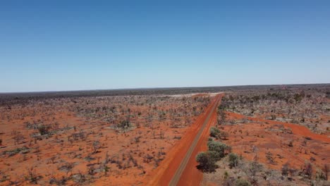 drone flying towards a sealed road and unsealed road intersection in the australian outback