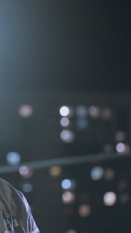 futbolista joven con guantes lanzando una pelota de fútbol en el aire y atrapándola contra un telón de fondo nocturno urbano, edificio borroso y efectos de luz bokeh brillantes