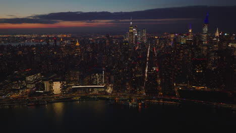 Aerial-panoramic-view-of-evening-skyline-with-illuminated-skyscrapers.-Heavy-traffic-on-waterfront-trunk-road.-Manhattan,-New-York-City,-USA