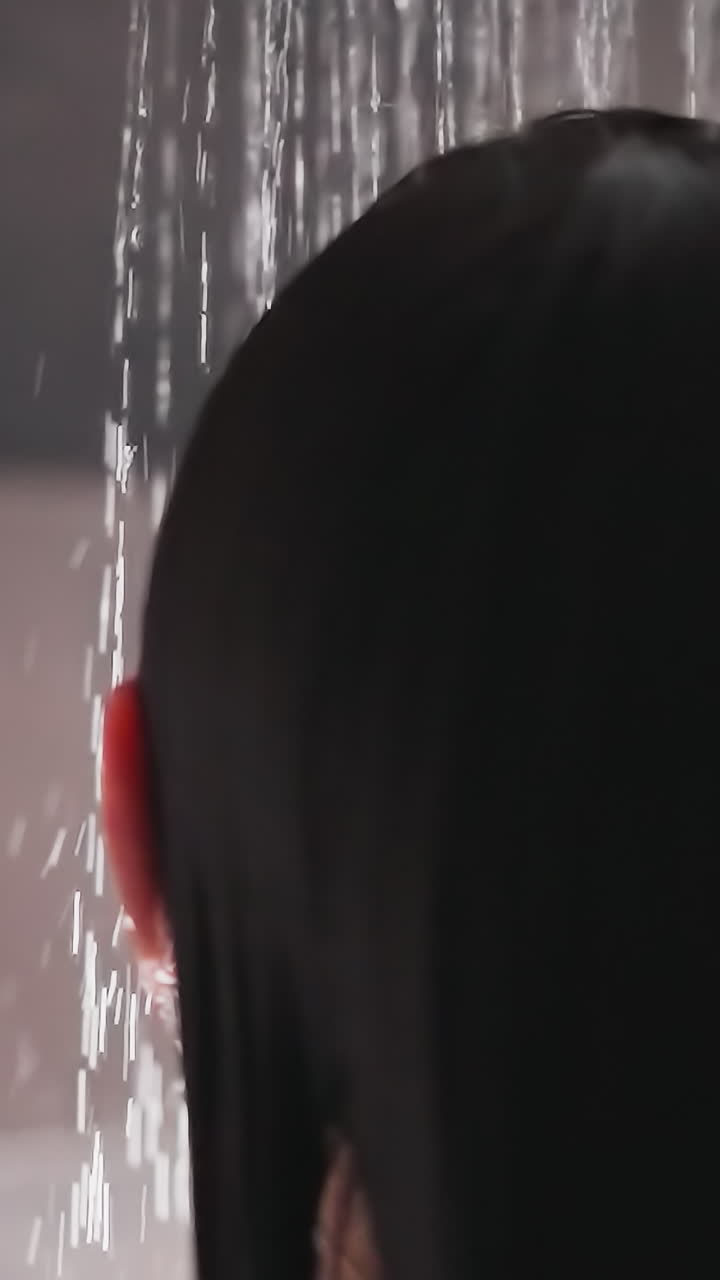 el agua cae en la cabeza fluyendo a lo largo del cabello de la dama. la mujer morena se lava la cabeza en el baño bajo corrientes de agua caliente. procedimientos de spa agradables en casa