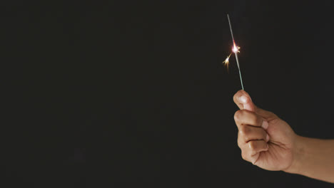 video of hand of african american person holding lit sparkler on black background, with copy space