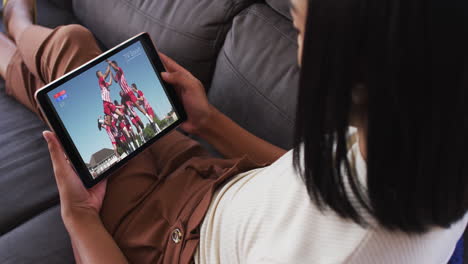 compuesto de una mujer en el sofá en casa viendo un evento deportivo en la tableta