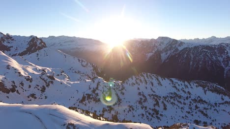 Snowed-Alps-in-the-Chamrousse-region-of-France-with-sunrise-between-rocky-peaks,-Aerial-pan-left-shot