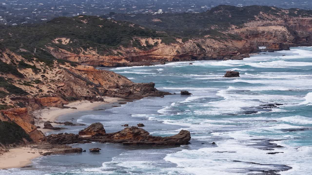 Aerial view of ocean waves hitting Sphinx Rock, rugged cliffs, and sandy beach at dusk