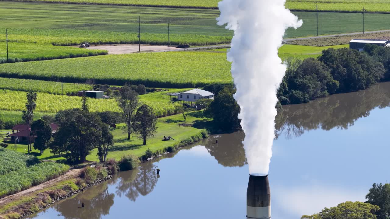 Drone footage captures a cooling tower releasing steam over a river in a lush, green landscape