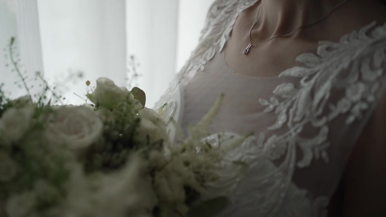 Primer plano de un vestido de encaje de novia y ramo bajo una iluminación suave, resaltando los detalles finos