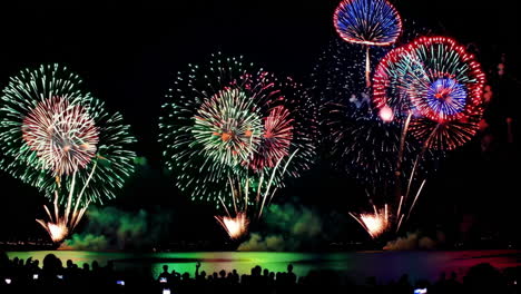 colorful fireworks display over water with crowd