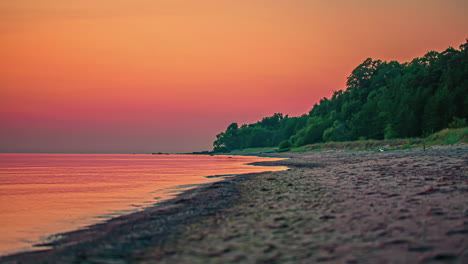 Orange-sunset-sky-reflects-off-the-surface-of-a-calm-ocean-at-the-beach---time-lapse