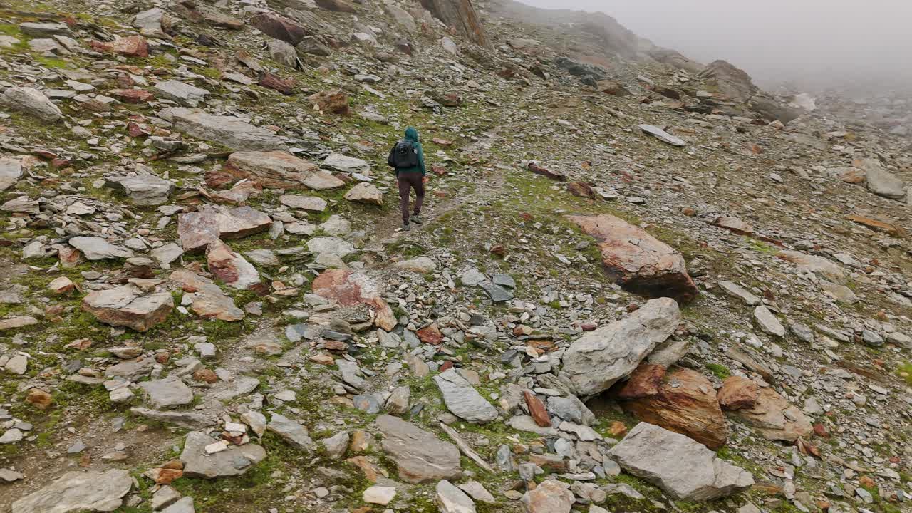 vista aérea de un excursionista solitario caminando por el camino en la ladera de una montaña rocosa a través de una niebla brumosa