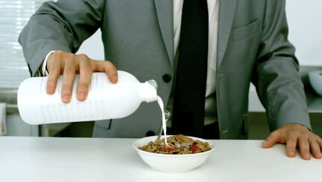 un hombre de negocios bien vestido vertiendo leche en sus cereales.