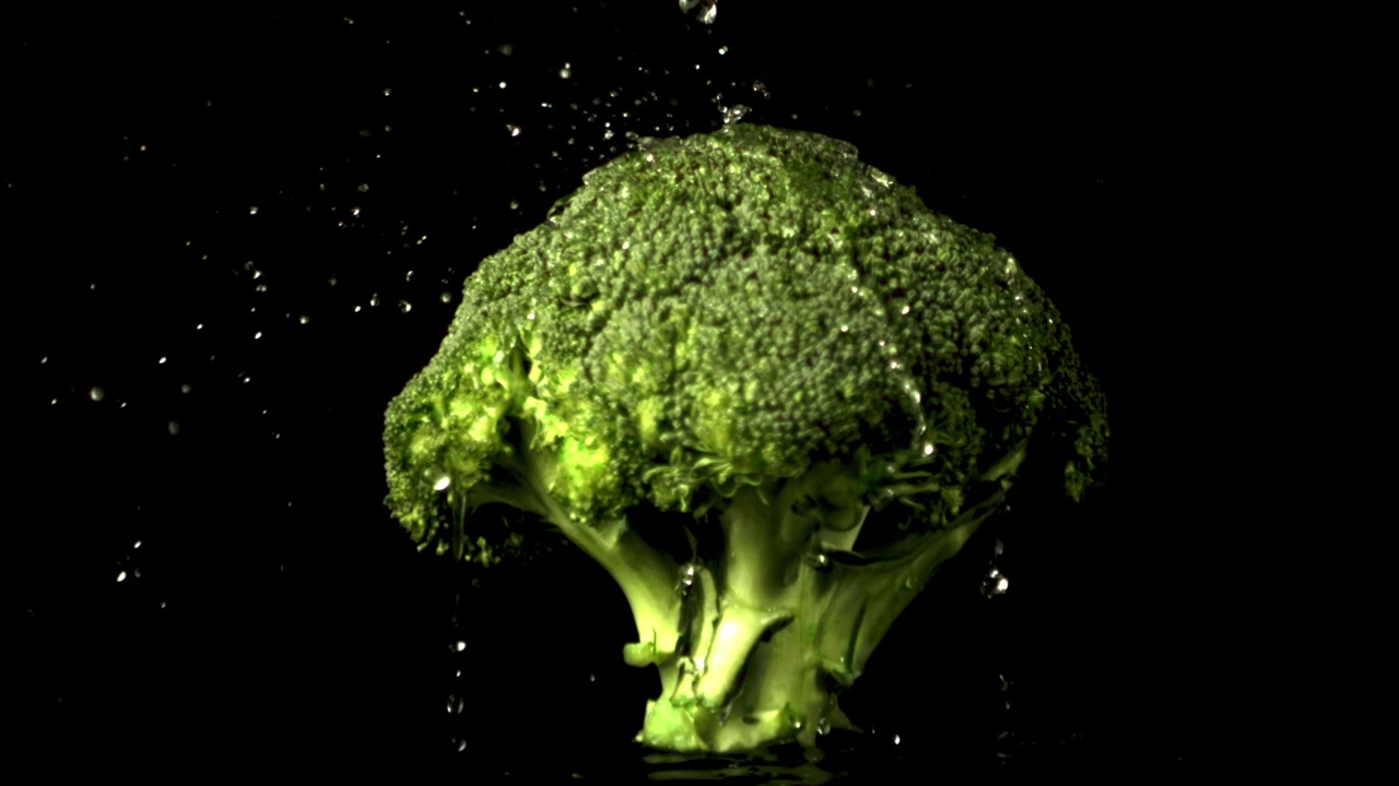 Gocce d'acqua che cadono su broccoli verdi freschi al rallentatore.
