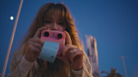 smiling girl instant camera taking picture cityscapes at night closeup.