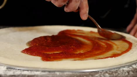 primer plano de poner salsa de tomate en la masa de la pizza