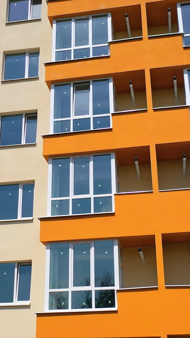 Modern high rise building with glazed balconies. Front view of newly built block of flats with colorful walls. New apartment building facade in the city. Vertical video