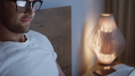 close-up view of smiling caucasian young man typing on the keyboard of the laptop late at night in the bed