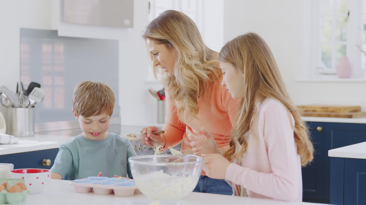 Mother Putting Cake Mixture On Son's Nose In Kitchen As They Have Fun Baking Cakes Together