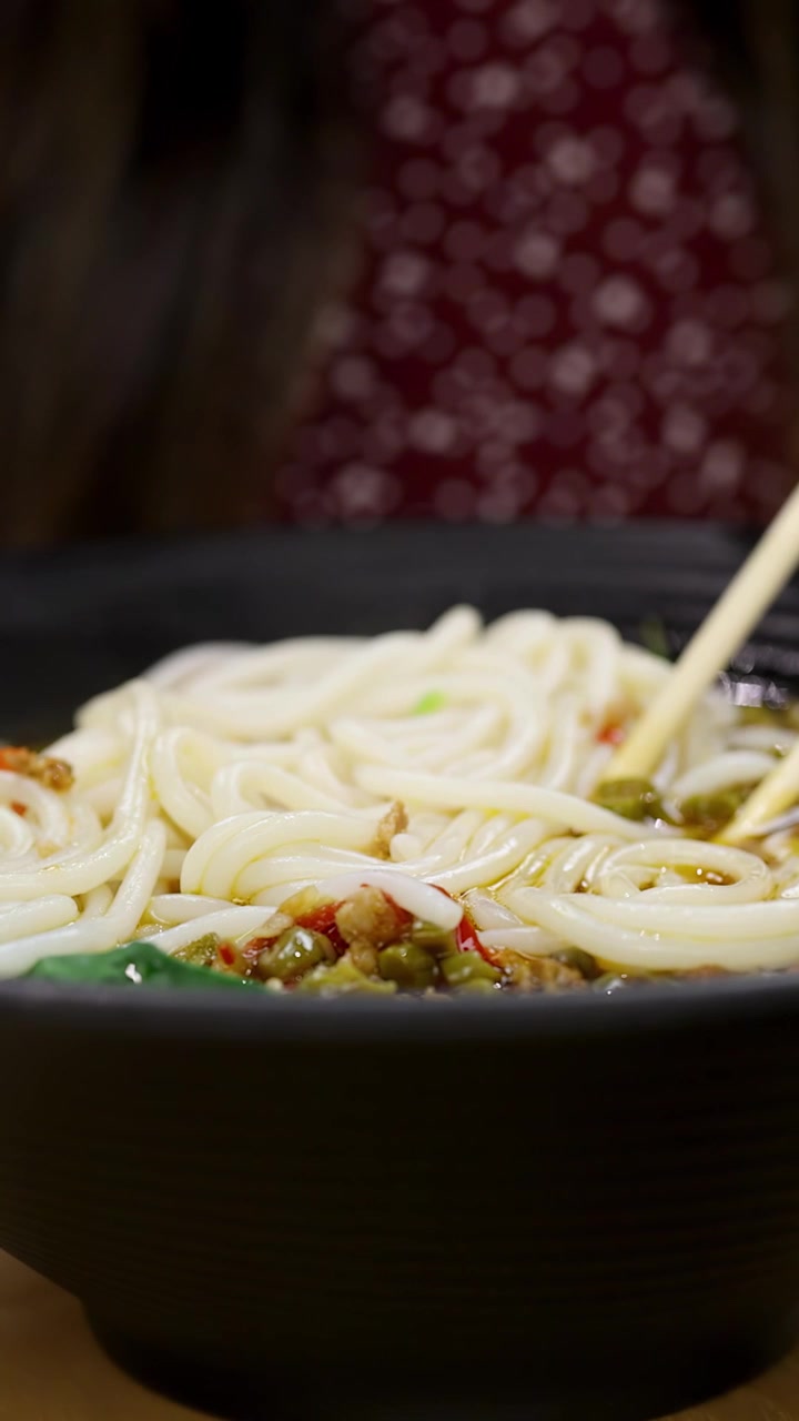 レストランで、黒いスプーンを使って湯気の立つスパイシーな麺スープをすくう手のクローズアップ。