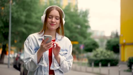 pretty young woman listening to music with wireless headphones and her smartphone while walking down the street