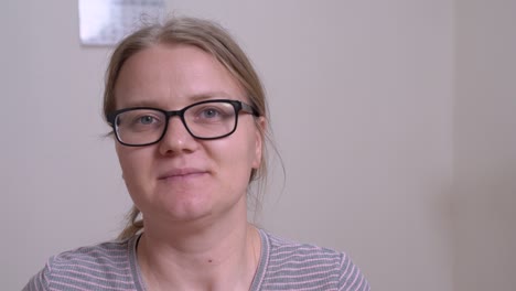 mujer joven con gafas hace un movimiento circular con el dedo índice cerca de su cabeza, con ironía o humor. en el interior, fondo gris claro.
