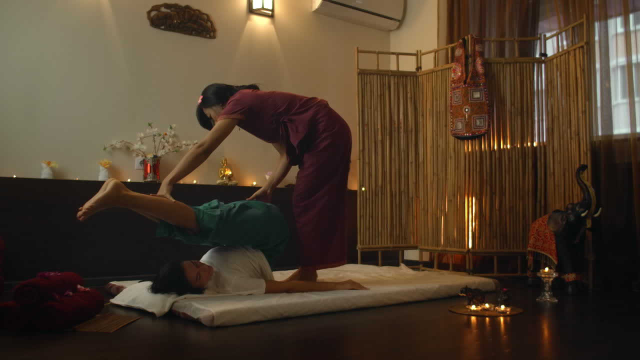 Asian Woman performs Traditional Thai Massage to beautiful European Woman. Rehabilitation and Treatment after Injuries with the help of Massage. Relax and Rest from massage of Legs Arms and Back. Therapeutic massage
