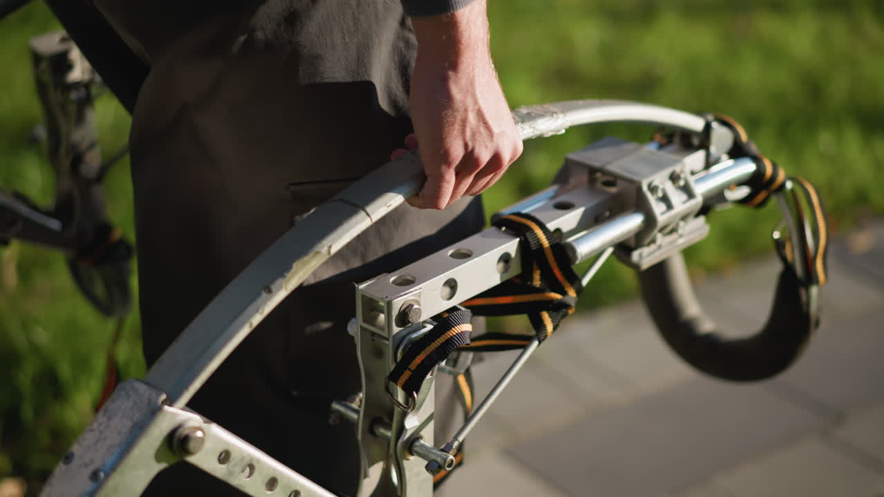 어두운 옷과 함께 금속 기 도구를 잡고 있는 사람의 클로즈업, 손과 장치에 초점을 맞춘 낮은 카메라 각도, 배경에 흐릿한 녹색 풀, 세부 사항을 강조하고, 움직임