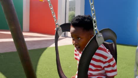 Side-view-of-African-American-schoolboy-playing-on-a-swing-in-school-playground-4k