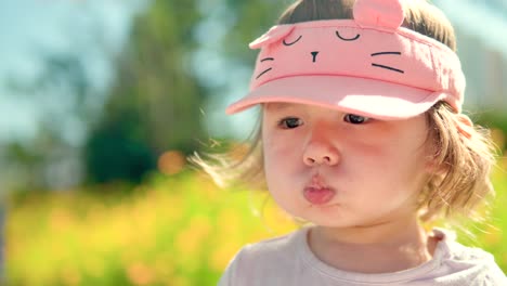 sleepy little girl holding water in the mouth and don't drink at the park with flowering yellow flowers - face close-up