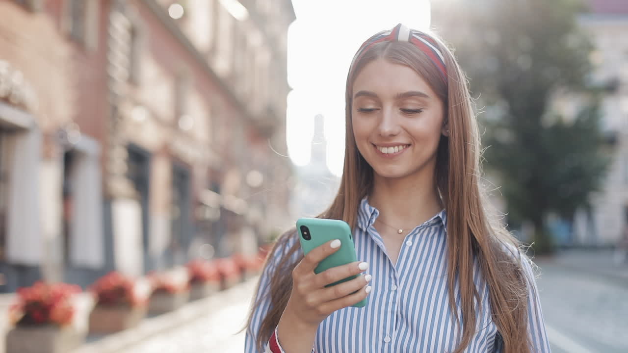 Jovem mulher feliz caminhando e usando smartphone na rua da cidade
