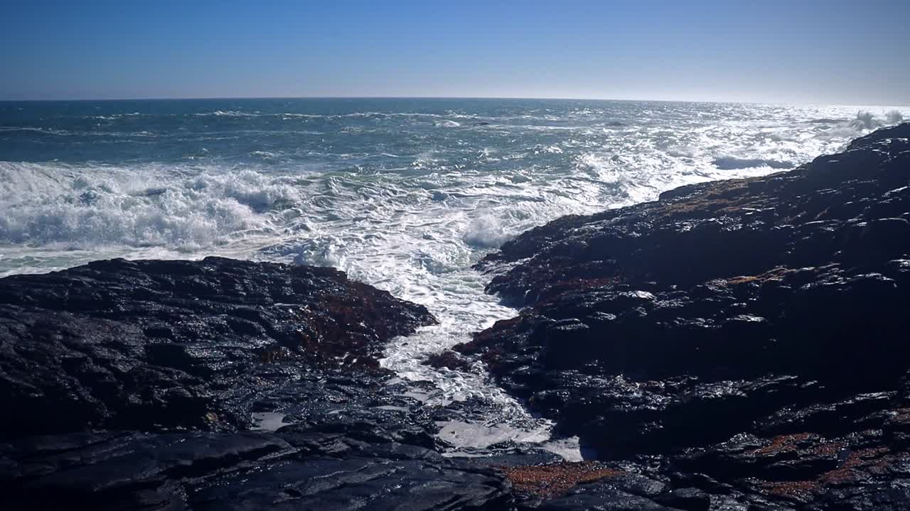 Escena a cámara lenta de potentes olas oceánicas rompiendo en un canal rocoso en Cornualles, Inglaterra, que muestra el flujo de agua blanca, la textura agitada del mar y la dramática energía costera.