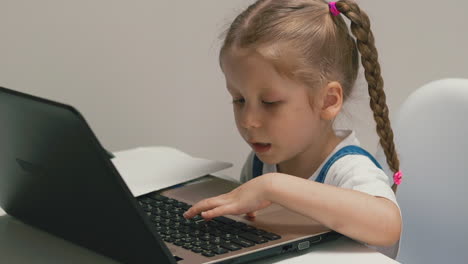 little girl plays on laptop at table in brightly lit room