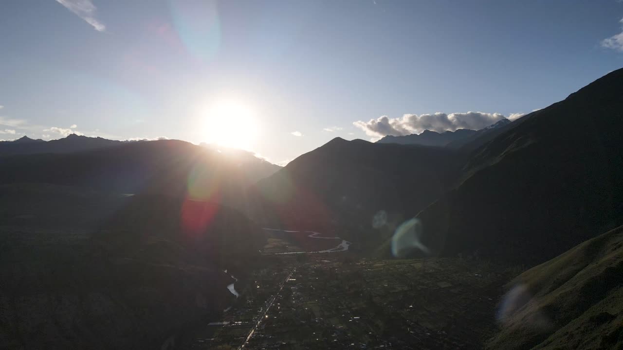 Aerial of the town and mountains of Urubamba, Sacred Valley, Cusco, Peru. Sun flare direct into lens. Drone slow orbit