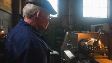 grey haired employee stands by operating lathe machine