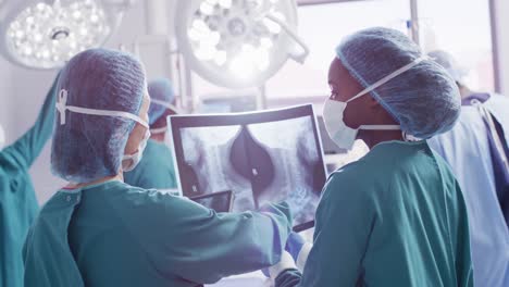 video of rear view of two diverse female surgeons discussing x-ray in operating theatre