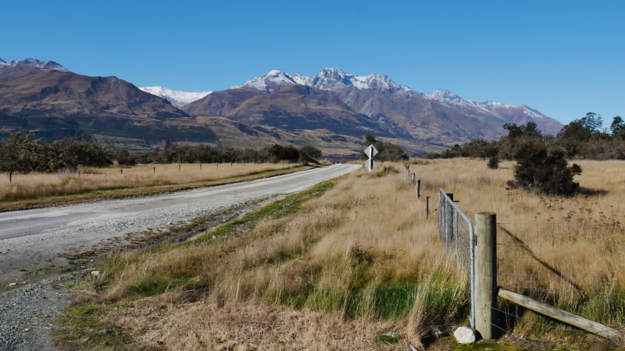 Panning shot of Glacier Burn Track with beautiful mountain range with snowy peaks - Beautiful sunny day with blue sky and lonely road in New Zealand