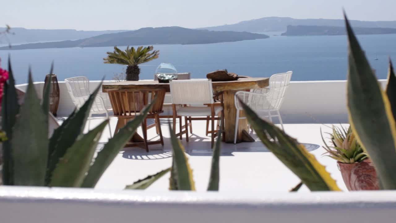 panorámica sobre flores de colores a través de una terraza con vistas al mar con muebles al aire libre en santorini, grecia