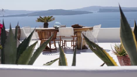 Panning-over-colorful-flowers-across-a-seaview-terrace-with-furniture-outdoors-in-Santorini,-Greece