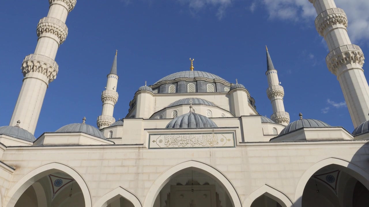 Low upward view of the Grand Mosque of Tirana with tall minarets and domes under a bright blue sky