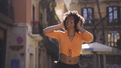 cheerful black woman dancing in headphones on street