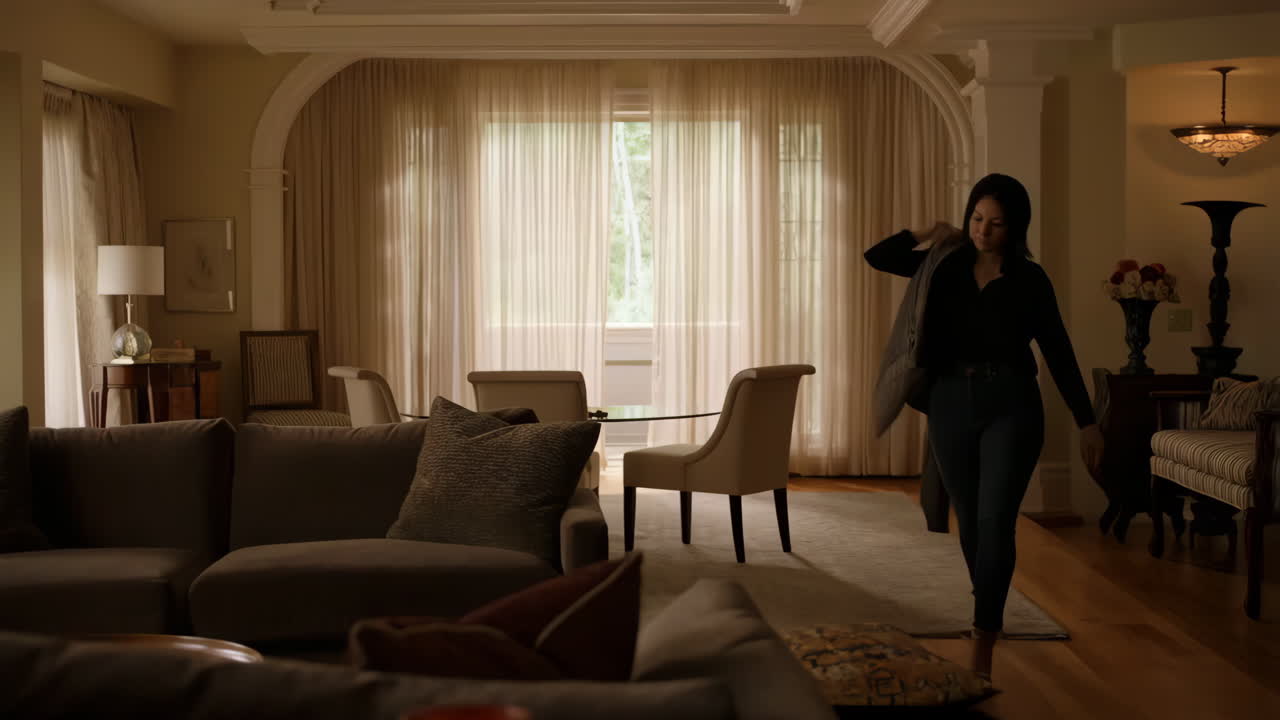 A woman throws a jacket onto a sofa in a modern living room